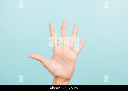 Gesto della mano. La mano femminile indica il numero cinque. Mano di donna che punta in su con tre dita su sfondo azzurro Foto Stock