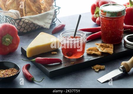 Un tavolo con gelatina di peperoncino piccante servito con cracker e formaggio, illuminato da dietro. Foto Stock