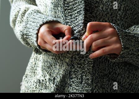 Primo piano di una giovane donna in cardigan di lana calda che si prepara per l'inverno freddo con carenza di gas ed elettricità a causa della guerra Russia Ucraina Foto Stock