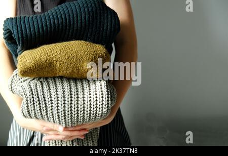 donna che tiene in mano la sua pila di caldi maglioni di lana e cardigan Foto Stock