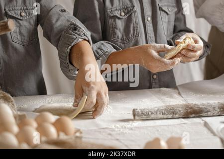 Le mani dei bambini, la farina e la pasta. I ragazzi stanno preparando un impasto per la cottura a casa. Concetto di cucina casalinga con ingredienti biologici e naturali. Zero wast Foto Stock