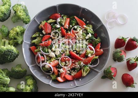 Broccoli con feta e fettine di fragole fresche. I fiori di broccoli saltati sono cosparsi di feta grattugiata e fragole fresche Foto Stock