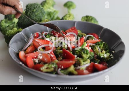 Broccoli con feta e fettine di fragole fresche. I fiori di broccoli saltati sono cosparsi di feta grattugiata e fragole fresche Foto Stock