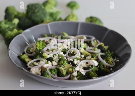 Broccoli con feta e anelli di cipolla. I fiori di broccoli saltati sono cosparsi di feta grattugiata e anelli di cipolla. Piatto sano a s Foto Stock