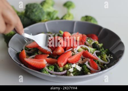 Broccoli con feta e fettine di fragole fresche. I fiori di broccoli saltati sono cosparsi di feta grattugiata e fragole fresche Foto Stock