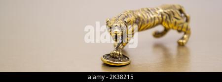 Banner con una figura di bronzo di una tigre con una moneta su uno sfondo dorato, copia spazio. Auguri di buona fortuna, benessere finanziario e ricchezza. Foto Stock