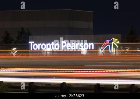 Il Toronto Pearson Intl. Il logo dell'aeroporto è visibile accanto a un'autostrada trafficata, illuminata di notte; i sentieri leggeri dei veicoli che passano illuminano. Foto Stock