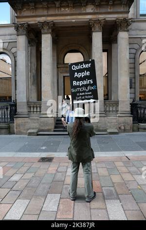 Buchanan Street, Glasgow, Scozia, Regno Unito. Un uomo si trova all'esterno del negozio Apple Store con un cartello che fa pubblicità alle riparazioni Apple più economiche Foto Stock