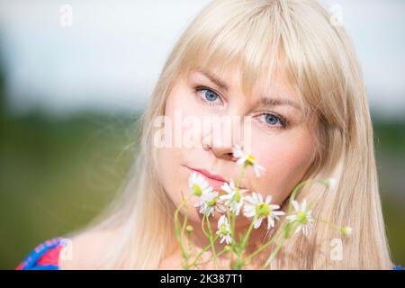 Ritratto di una donna di mezza età con capelli bianchi che tiene un bouquet di margherite di campo. Foto Stock