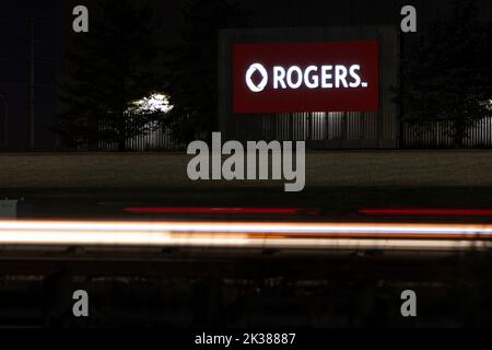 Il logo Rogers è illuminato su un cartello, visto di notte lungo una strada trafficata; Rogers è il più grande gestore wireless del Canada e una società di media. Foto Stock