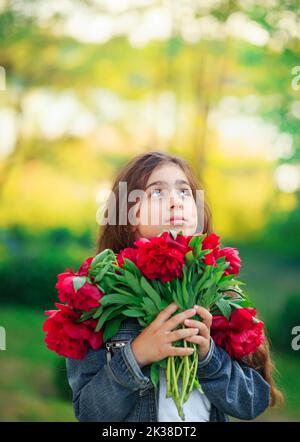 Piccola ragazza carina con fiori di peonia. Bambini che giocano nel giardino estivo. Giardinaggio per bambini. I bambini giocano all'aperto. Bimbo toddler con bouquet di fiori per uccelli Foto Stock