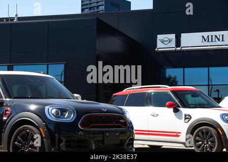 Il logo e il cartello Mini sono visti in cima a una concessionaria Mini con le nuove auto parcheggiate davanti. Mini è un produttore britannico storico, ora di proprietà tedesca. Foto Stock