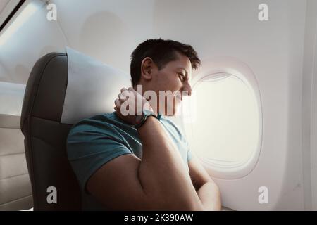 Un uomo soffre di un forte dolore al collo durante un lungo volo in una posizione scomoda su un aereo. Osteocondrosi sintomi e cause Foto Stock