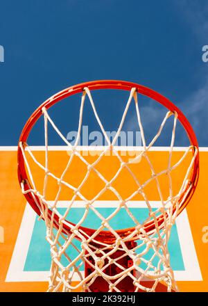 Colorato backboard arancione da basket con cerchio rosso e una rete contro il cielo blu vista angolo basso con spazio copia Foto Stock