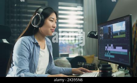 Freelancer asiatico femminile di editing video per il cliente o di viaggio blogger in programma sul computer, mentre si siede al tavolo e di lavoro a casa Foto Stock
