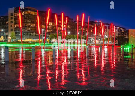 Dublino, Irlanda, agosto 2019 bastoni rossi sulla Grand Canal Square in docklands a pioggia, notte o ora blu. Negozi ed edifici di appartamenti sullo sfondo Foto Stock