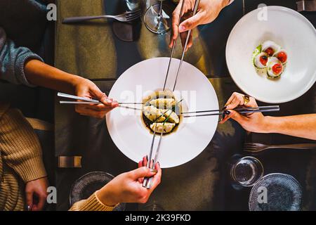 Gruppo di amici che raccolgono un gyoza tradizionale gnunpling in un ristorante fusion giapponese - vista piatto - persone che condividono il cibo in un ristorante asiatico - p Foto Stock