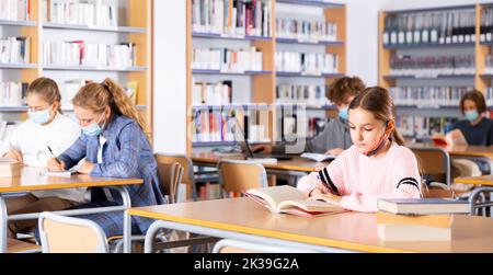 Adolescenti in maschere che trascorrono del tempo in biblioteca Foto Stock