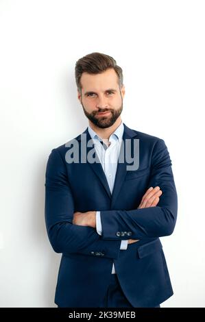 Foto verticale di un uomo d'affari caucasico orgoglioso e fiducioso, dirigente aziendale, in tuta formale ed elegante, in piedi su sfondo bianco isolato con braccia incrociate, guarda la macchina fotografica, sorridendo Foto Stock