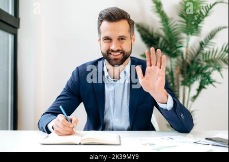 Uomo d'affari professionale caucasico positivo, mentore, agitare la mano e guardare la webcam durante la videoconferenza, ascoltare la lezione, webinar leader, registrare la formazione online, sorridere amichevole Foto Stock