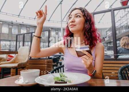 la ragazza ha alzato la mano e chiama il cameriere a pagare la colazione nel bar con una carta Foto Stock