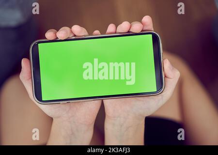 Primo piano delle mani dei bambini utilizzando un telefono con schermo verde. Una bambina è seduta sul pavimento e tiene in mano uno smartphone con un tasto colorato. Foto di alta qualità Foto Stock