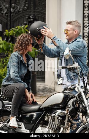 Uomo sorridente maturo che aiuta la ragazza a indossare il casco da motocicletta Foto Stock