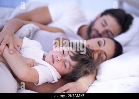 Vuole essere sempre vicino alla mamma e al papà, una giovane famiglia a letto insieme. Foto Stock