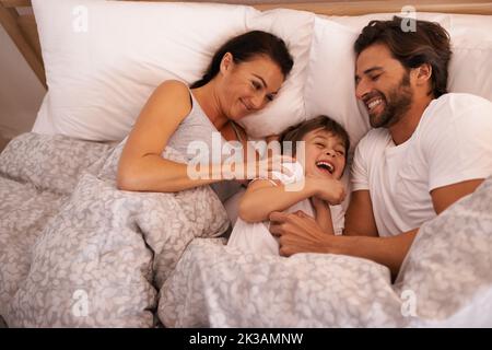 Vuole essere sempre vicino alla mamma e al papà, una giovane famiglia a letto insieme. Foto Stock