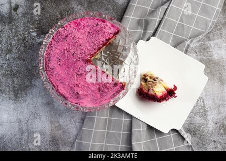 Insalata russa - aringhe sotto un cappotto di pelliccia, insalata di aringhe con patate, uova, barbabietole, carote e maionese su un piatto quadrato bianco su un backgro scuro Foto Stock