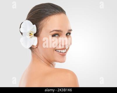 Perfezionare la perfezione. Studio beauty shot di una bella donna brunetta con un fiore nei suoi capelli. Foto Stock