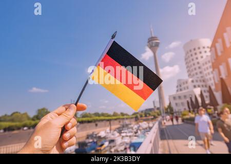 Bandiera nazionale tedesca in mano al Media Harbor e alla torre della televisione a Dusseldorf. Studiare la lingua all'estero e il concetto di viaggio Foto Stock