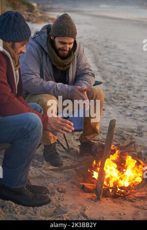 Riscaldamento a causa del fuoco. Due giovani seduti attorno ad un fuoco sulla spiaggia. Foto Stock