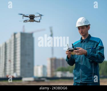 Un uomo in un casco e tute controlla un drone in un cantiere. Il costruttore esegue la supervisione tecnica. Foto Stock