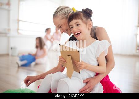 Felice ragazza disabile coccole con la madre e guardando la foto durante la lezione di balletto. Concetto di integrazione dei bambini disabili e della paternità. Foto Stock