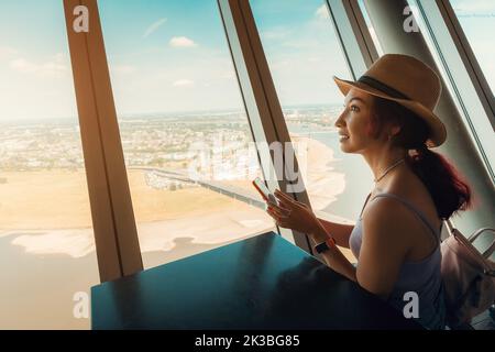 Una ragazza felice guarda e ammira dalla finestra sul ponte di osservazione della torre della televisione di Dusseldorf. Grande punto di vista per i turisti in Germania Foto Stock