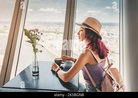 Una ragazza felice beve un caffè in un bar e ammira dalla finestra sulla terrazza panoramica della torre della televisione di Dusseldorf. Grande punto di vista per i turisti Foto Stock