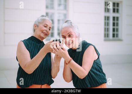 Donne anziane gemellano all'aperto in uno smartphone per il controllo della città. Foto Stock