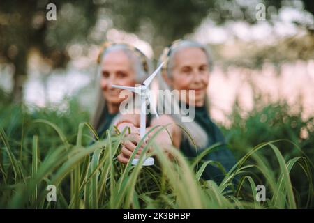 Donne anziane, gemelle che detengono il modello plastico della turbina eolica in natura, concetto di futuro, ecologia e risorse rinnovabili, messaggio per la prossima generazione. Foto Stock