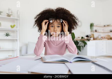 Scioccato scolaro bambino nero che fa i compiti a casa Foto Stock