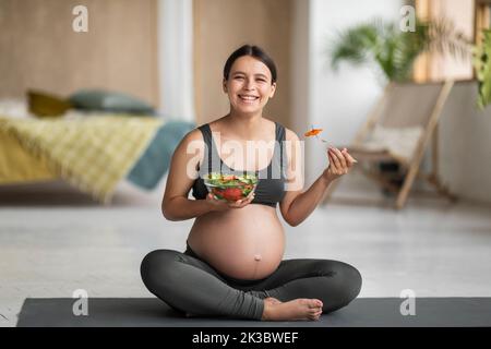 Dieta di gravidanza. Felice giovane donna incinta mangiare insalata di verdure fresche a casa Foto Stock