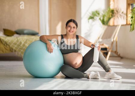Esercizio fisico e gravidanza. Bella donna incinta in Activewear seduta vicino a Big Fitball Foto Stock