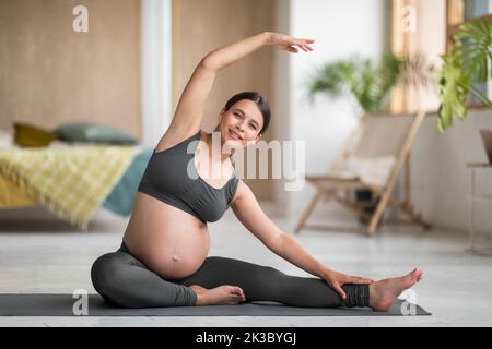 Ritratto di sorridente bella donna incinta fare ginnastica Prenatale a casa Foto Stock