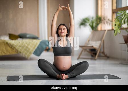 Gravidanza Yoga. Calma bella donna incinta stretching su tappetino fitness a casa Foto Stock