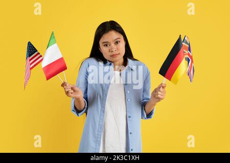Triste confuso giovane studentessa cinese in casual con molte bandiere diverse guardare la fotocamera Foto Stock
