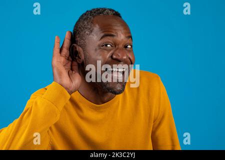 Un uomo nero eccitato che tiene la mano accanto all'orecchio e sorrida Foto Stock