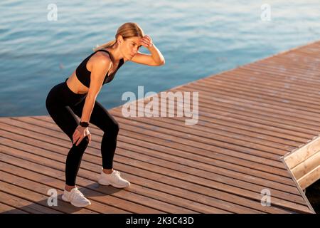 Stanco anziano giogro femminile di mezza età riposante dopo la corsa sul molo vicino al fiume Foto Stock