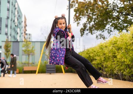 Ragazza sorridente che oscilla su una corda in un parco giochi Foto Stock