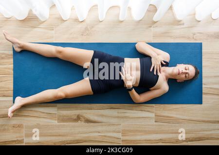 Giovane donna che si rilassa in shavasana o in corpse yoga posa dopo il suo allenamento mattutino Foto Stock