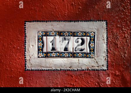Targa vintage 172 in ceramica e attaccata alla parete rossa della casa Foto Stock